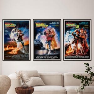 Può includere: Tre poster cinematografici incorniciati della serie di film Ritorno al Futuro. I poster presentano opere d'arte vibranti con i titoli dei film e i nomi degli attori. I poster sono esposti sopra un divano bianco.