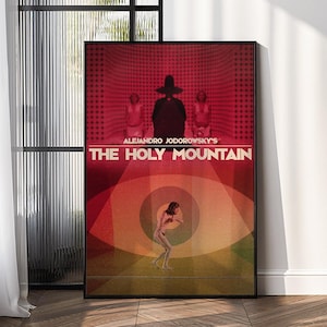 May include: A framed movie poster for "The Holy Mountain" by Alejandro Jodorowsky. The poster features a red and orange color scheme with the film's title in large white letters. The image includes figures and an eye design.
