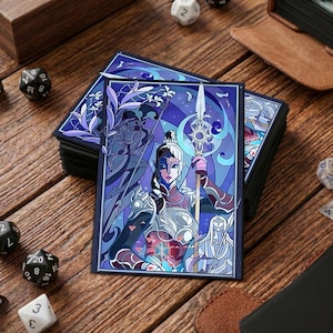 May include: A stack of card sleeves with a stained-glass style illustration of a fantasy warrior holding a spear. The artwork is mainly purple, blue, and red, with white accents. Dice and a leather-bound book are in the background.