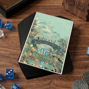 May include: A stack of black card sleeves with a colorful illustration of a scene from Lord of the Rings. The artwork depicts a bridge with figures, waterfalls, and a building. Dice and metal coins are scattered around.