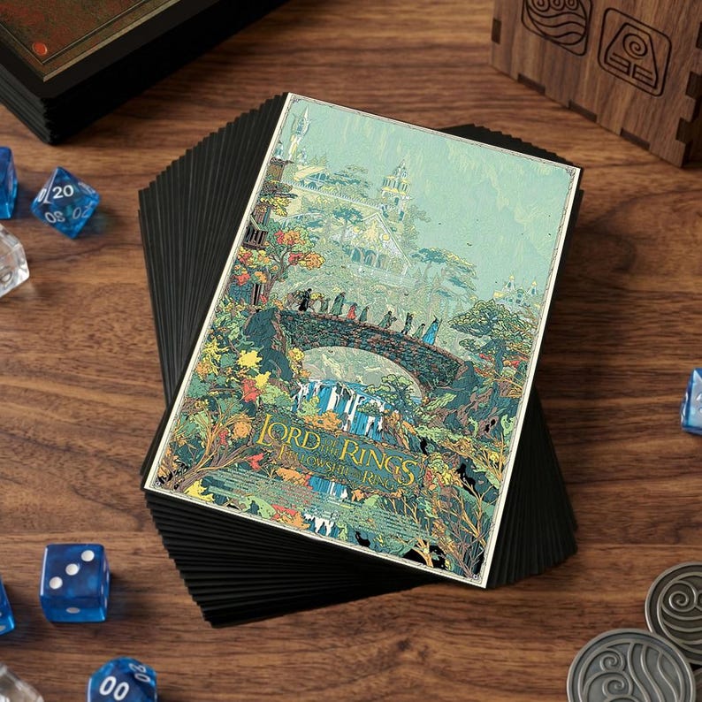 May include: A stack of black card sleeves with a colorful illustration of a scene from Lord of the Rings. The artwork depicts a bridge with figures, waterfalls, and a building. Dice and metal coins are scattered around.
