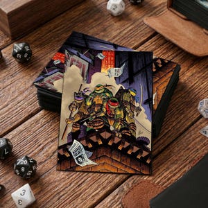 Op de afbeelding: Kaarthoesjes met de Teenage Mutant Ninja Turtles op een dak, met een stadslandschap op de achtergrond. De afbeelding bevat de tekst "Masked Vigilante" op een krant. De kaarthoesjes liggen op een houten oppervlak met dobbelstenen.