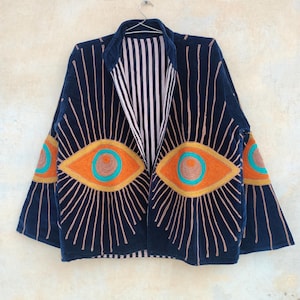 Puede incluir: Chaqueta azul marino con diseños de ojos bordados en naranja, turquesa y marrón. La chaqueta presenta líneas verticales y un forro interior a rayas. Las mangas también tienen diseños de ojos.