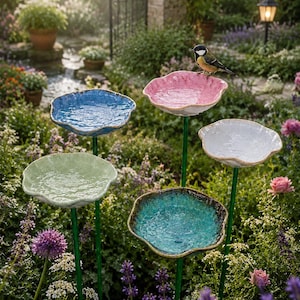 Peut inclure: Un ensemble de cinq abreuvoirs à oiseaux de jardin sur de fines tiges métalliques vertes. Chaque abreuvoir présente un bol peu profond, festonné et de style céramique, dans des couleurs distinctes : rose, bleu, blanc, vert clair et sarcelle.