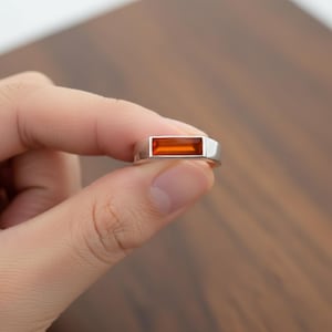 May include: A silver ring with a rectangular, orange gemstone. The ring's band is a simple, modern design, and the gemstone is set flush within the ring's face. The ring is held between fingers against a wooden background.