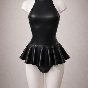 May include: Black latex bodysuit with a high neck and halter-style top. The garment features a flared skirt detail at the waist and is displayed on a white mannequin. The overall style is sleek and modern.
