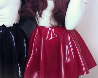 May include: Two individuals pose, each wearing a unique headpiece with radiating spikes. One wears a black skirt and the other a red skirt. Both wear white tops. The image has a gothic aesthetic.