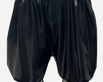 May include: Black latex bloomers featuring a high-waisted design with a wide, light-colored waistband. The garment has a voluminous, gathered silhouette with pleated leg openings finished with a light-colored trim and a ruffled black edge.