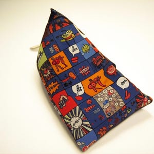 May include: A triangular-shaped pillow with a vibrant comic book-style pattern. The design features a blue background with colorful squares containing various illustrations and speech bubbles. The pillow is likely used for neck support.