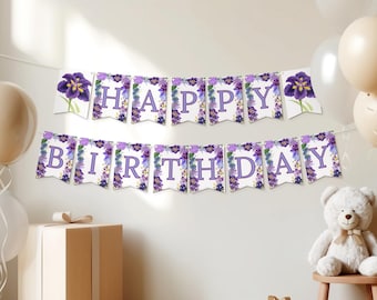 May include: A "Happy Birthday" banner with purple lettering and floral accents. The banner is strung across a white wall, with balloons and a teddy bear in the background. A gift box is in the foreground.