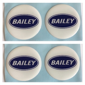Könnte beinhalten: Vier weiße, kreisförmige Aufkleber mit dem Namen "BAILEY" in Marineblau, innerhalb eines Ovals, auf hellblauem Hintergrund. Die Aufkleber sind in zwei Reihen zu je zwei angeordnet.
