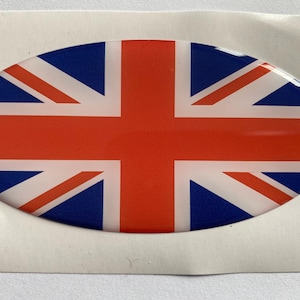 Puede incluir: Una pegatina ovalada con la Union Jack, la bandera del Reino Unido. El diseño incluye los colores rojo, blanco y azul, con un acabado brillante. La pegatina está sobre un fondo blanco.