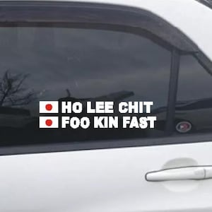 May include: White car window decal with the text "HO LEE CHIT FOO KIN FAST" in a bold, sans-serif font. The decal includes two small Japanese flags. The decal is applied to the rear window of a white car.