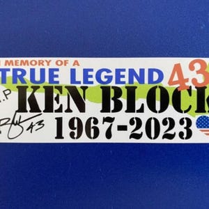 Op de afbeelding: Een rechthoekige sticker met tekst ter ere van Ken Block. De sticker leest "IN MEMORY OF A TRUE LEGEND 43 KEN BLOCK 1967-2023" met "R.I.P." en een handtekening. Het ontwerp bevat een groene en gele kaartomtrek en een hart met een Amerikaanse vlag.