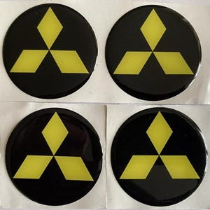 May include: Four round black stickers with a yellow three-diamond logo. The stickers are on a white backing. The logo is a stylized representation of three diamonds arranged in a triangular pattern.