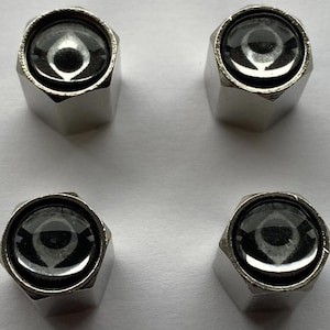 May include: Four silver-colored, hexagonal tire valve stem caps with a dark, reflective, circular top. The caps are arranged in a square formation against a light background. The reflective tops have a circular design.