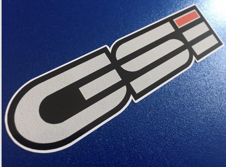 May include: A sticker featuring a graphic design in grey, black, and red. The design includes the letters "GE" in a bold font, with a red rectangular accent. The sticker has a white border and is on a blue background.