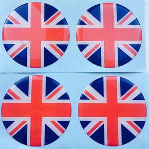 Puede incluir: Cuatro pegatinas redondas con el diseño de la bandera del Reino Unido. Cada pegatina tiene un borde azul, una cruz roja y rayas diagonales blancas y rojas. Las pegatinas están dispuestas sobre una superficie azul claro.