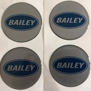 Könnte beinhalten: Vier graue, kreisförmige Aufkleber mit dem Wort "BAILEY" in einem blauen Oval. Die Aufkleber sind in einem 2x2-Raster auf weißem Hintergrund angeordnet. Der Text ist in einer serifenlosen Schriftart.
