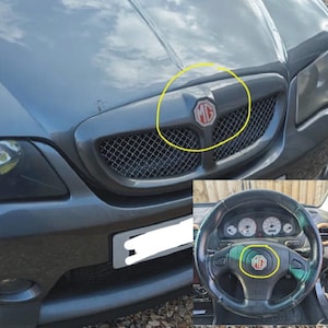 Puede incluir: Primer plano de la parrilla delantera y el volante de un coche gris. La parrilla presenta un diseño de malla con el logotipo "MG" rojo y blanco. El volante también muestra el logotipo "MG" en el centro.