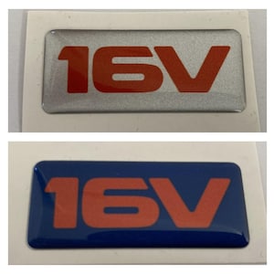 May include: Two rectangular car emblems. The top emblem is silver with the red text "16V". The bottom emblem is blue with the same red "16V" text. Both emblems are on a white background.