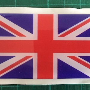 Puede incluir: Una pegatina rectangular con la Union Jack, la bandera del Reino Unido. El diseño presenta una cruz roja y rayas diagonales sobre un fondo blanco, sobre un fondo azul.