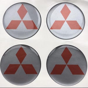 May include: Four circular stickers featuring the Mitsubishi logo. Each sticker has a silver-gray background with a red three-diamond emblem in the center. The stickers are glossy and appear to be new.
