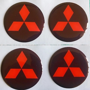 May include: Four circular stickers featuring the Mitsubishi logo. Each sticker has a dark brown background with a bright red three-diamond emblem in the center. The stickers are arranged in a 2x2 grid.