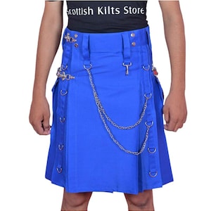 Puede incluir: Un kilt azul brillante con detalles metálicos plateados, que incluyen cadenas y anillas en D. El kilt presenta pliegues y un cierre en forma de llave. El texto "Scottish Kilts Store" es visible en una camiseta negra.