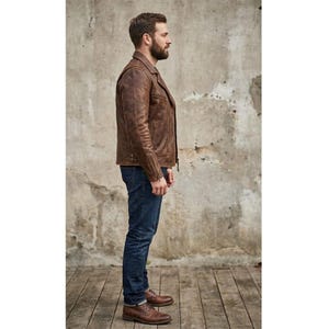 K&ouml;nnte beinhalten: Braune Lederjacke mit klassischem Design, mit Reverskragen, Rei&szlig;verschluss und mehreren Taschen. Die Jacke wird mit blauen Jeans und braunen Lederschuhen kombiniert. Das Outfit wird vor einem neutralen Hintergrund pr&auml;sentiert.