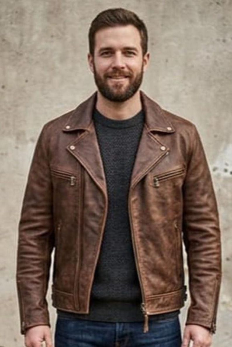 K&ouml;nnte beinhalten: Braune Lederjacke im klassischen Biker-Stil. Die Jacke hat einen Reverskragen, einen asymmetrischen Rei&szlig;verschluss und mehrere Taschen. Das Model tr&auml;gt einen dunkelgrauen Pullover darunter. Die Jacke scheint aus hochwertigem Leder zu sein.