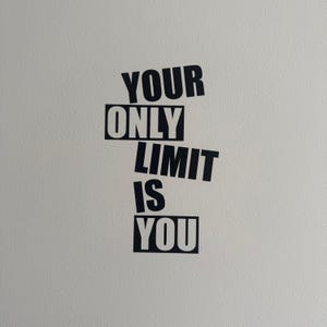 Könnte beinhalten: Schwarzer Text auf einer weißen Wand mit der Aufschrift "YOUR ONLY LIMIT IS YOU". Die Wörter sind in einem gestapelten, leicht abgewinkelten Design angeordnet. Die Wand hat eine strukturierte Oberfläche.