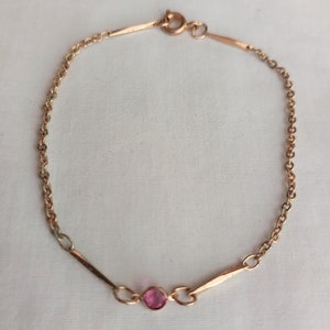 Puede incluir: Un brazalete de cadena de oro con una piedra preciosa rosa en el centro.