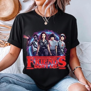 May include: Black t-shirt featuring a graphic of four characters with a neon blue and purple background. The text "FRIENDS DON'T LIE" is in red. The design is centered on the shirt.