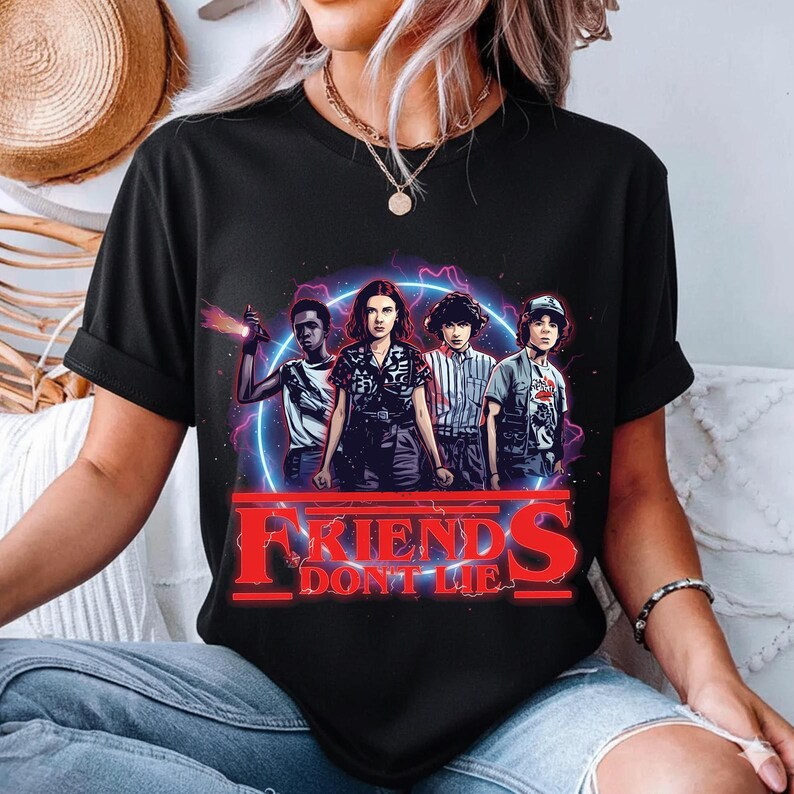 May include: Black t-shirt featuring a graphic of four characters with a neon blue and purple background. The text "FRIENDS DON'T LIE" is in red. The design is centered on the shirt.