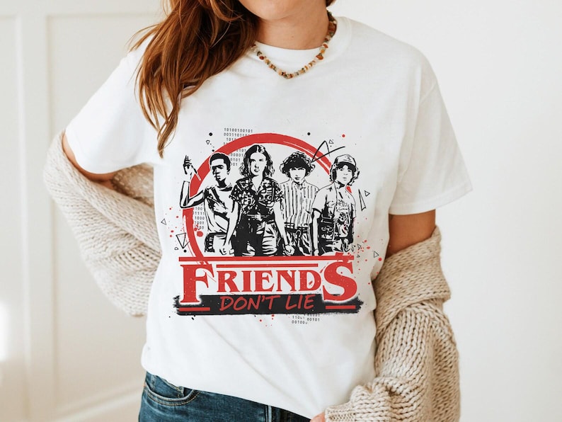 May include: White t-shirt featuring a graphic of four characters inside a red circle, with the words "FRIENDS DON'T LIE" in red and black. The design is a reference to a popular science fiction series.