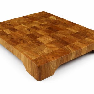 May include: A rectangular end-grain butcher block cutting board made of light brown wood. The board has a mosaic pattern and curved edges with a handle cutout on each end. This kitchen item is ideal for food preparation.