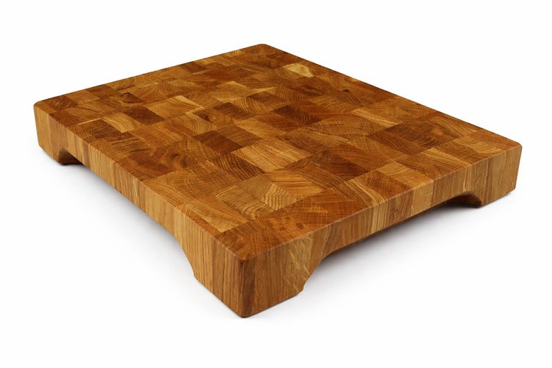 May include: A rectangular end-grain butcher block cutting board made of light brown wood. The board has a mosaic pattern and curved edges with a handle cutout on each end. This kitchen item is ideal for food preparation.