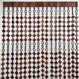 Pode incluir: Uma cortina decorativa de contas de madeira com um padrão repetitivo de trevos de quatro folhas em tons variados de castanho. A cortina é suspensa de uma cabeceira de madeira com anéis e correntes de metal, criando uma estética rústica e natural.