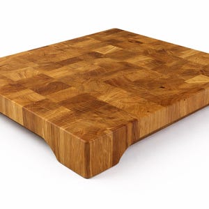 May include: A rectangular end-grain butcher block cutting board made of light brown wood. The board has a thick, solid construction with a mosaic-like pattern on the surface. It features curved cutouts on the sides for easy handling.
