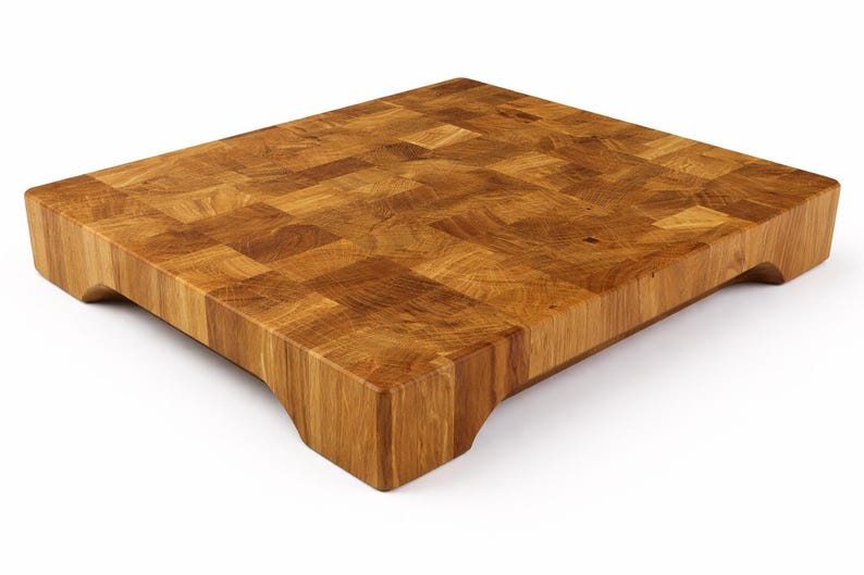 May include: A rectangular end-grain butcher block cutting board made of light brown wood. The board has a thick, solid construction with a mosaic-like pattern on the surface. It features curved cutouts on the sides for easy handling.