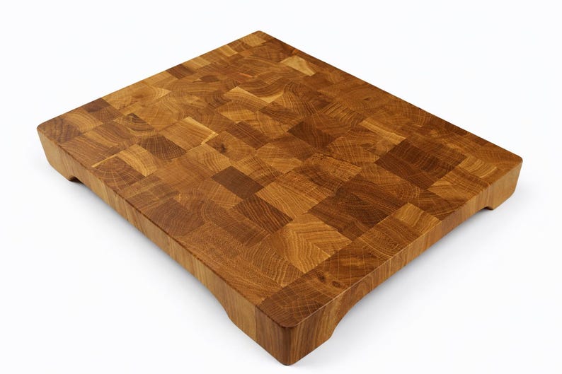 May include: A square, end-grain butcher block cutting board made of light and dark brown wood. The board has a mosaic-like pattern and is raised slightly off the surface with small feet. This durable board is ideal for food preparation.