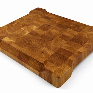 May include: A square, end-grain butcher block cutting board made of light brown wood. The board has a mosaic-like pattern and rounded corners with finger grips. The wood grain is visible throughout the board, which is ideal for kitchen use.