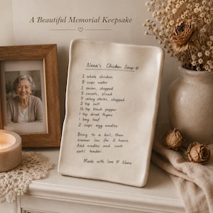 May include: A rectangular, off-white ceramic tray featuring the handwritten recipe for Nana's Chicken Soup in black ink. The text lists ingredients including chicken, water, onion, carrots, celery, salt, pepper, thyme, bay leaf, and egg noodles.