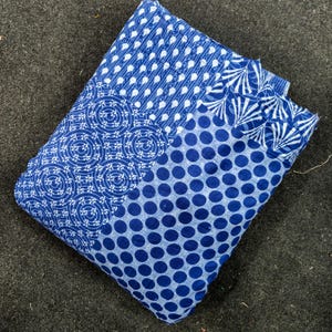 Può includere: Un tessuto piegato caratterizzato da un design patchwork con vari motivi in blu e bianco. Il tessuto mostra sezioni a pois blu scuro, intricati motivi geometrici circolari e forme a foglia ripetute, il tutto cucito insieme.