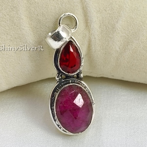 Puede incluir: Colgante de plata con dos piedras preciosas. La piedra superior es una piedra roja oscura en forma de lágrima. La piedra inferior es una piedra rosa oscuro de forma ovalada. El colgante tiene un lazo en la parte superior para una cadena.
