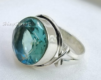 May include: A close-up of a silver ring featuring a large, faceted, oval-shaped, light blue gemstone. The ring has a thick band with decorative silver accents. The ring is displayed on a white surface. The text "ShinySilverR" is visible.