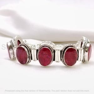 Puede incluir: Una pulsera de eslabones de plata con varias piedras preciosas ovaladas de color rojo intenso engastadas en marcos de metal pulido. Cada piedra está rodeada por un borde de cuerda trenzada y unida por barras de plata.
