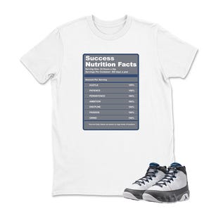 May include: White t-shirt with a "Success Nutrition Facts" graphic. The graphic resembles a nutrition label, listing qualities like "Hustle," "Patience," and "Persistence" at 100%. A pair of gray and black sneakers with blue accents are at the bottom.