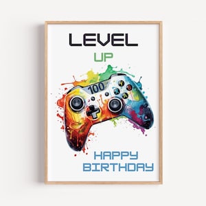 Könnte beinhalten: Ein gerahmter Druck mit einem farbenfrohen Videospiel-Controller im Aquarellstil. Der Controller ist mit roten, orangefarbenen, gelben, grünen und blauen Farbspritzern verziert. Der Text enthält "LEVEL UP", "100" und "HAPPY BIRTHDAY."
